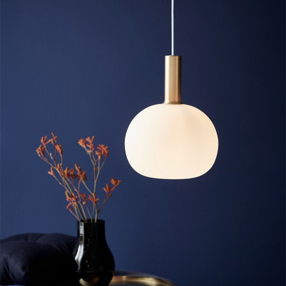 Selma round opal glass pendant with brass cap above a vase