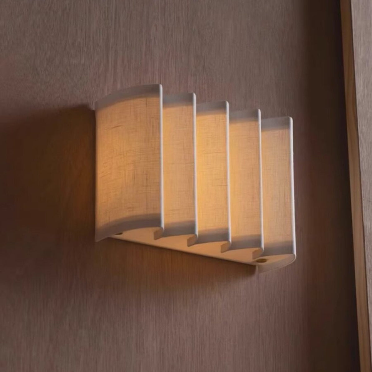 Wave pleated linen wall lamp glowing warm on a wood panel wall