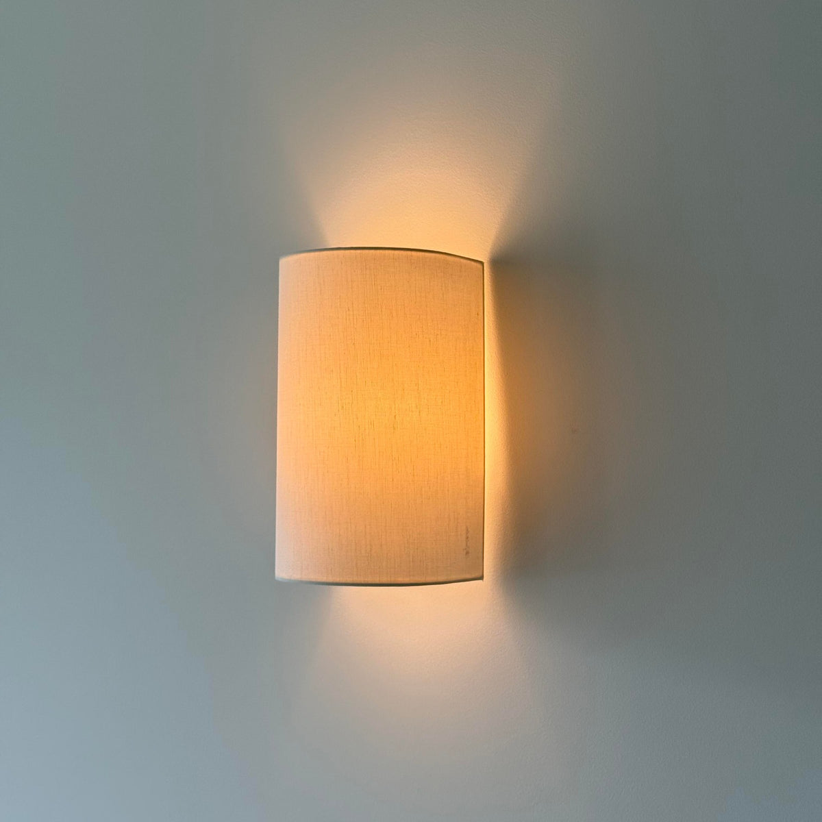 Half-round linen wall lamp glowing warm on a soft blue wall