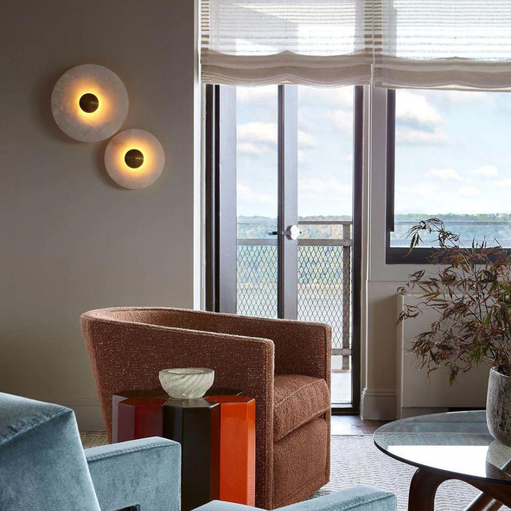 Two illuminated alabaster disc wall lights beside a window in a furnished living room