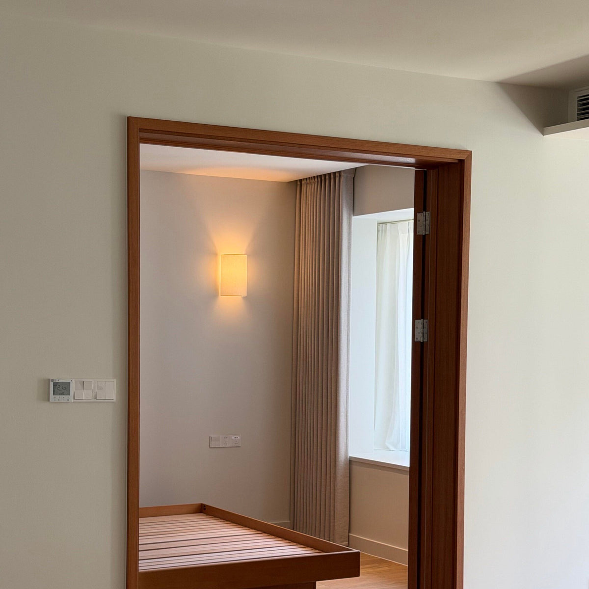 Fabric wall lamp glowing in a bedroom seen through a doorway